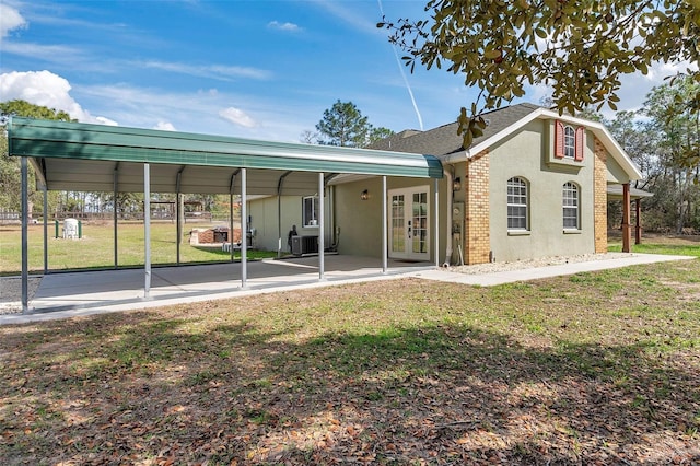 back of property with central AC unit, a lawn, a detached carport, french doors, and stucco siding