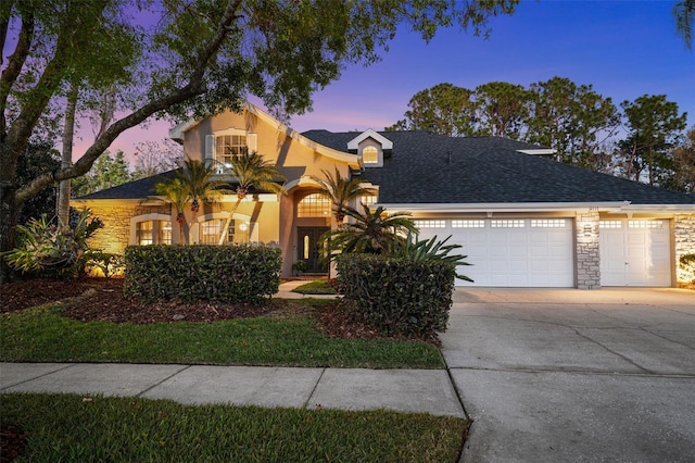 view of front of property with stucco siding, driveway, stone siding, roof with shingles, and an attached garage