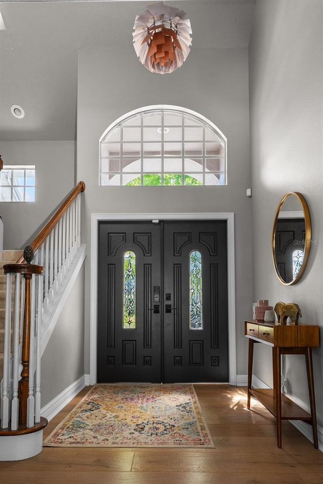 entryway with stairs, wood-type flooring, baseboards, and a towering ceiling