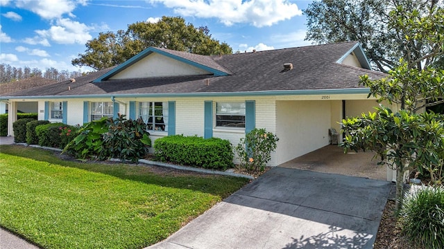 view of front of property with a shingled roof, concrete driveway, an attached carport, a front lawn, and brick siding