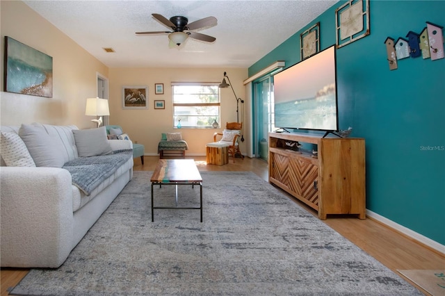 living room with baseboards, a textured ceiling, visible vents, and wood finished floors