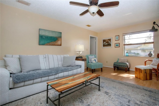 living room with a textured ceiling, wood finished floors, visible vents, baseboards, and a ceiling fan