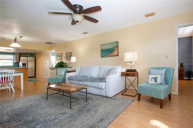 living area with light wood-type flooring, visible vents, and a textured ceiling