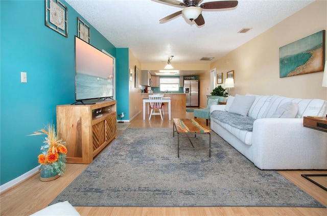 living area featuring light wood-style floors, ceiling fan, visible vents, and a textured ceiling