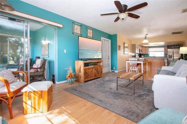 living area with light wood finished floors, visible vents, baseboards, ceiling fan, and a textured ceiling