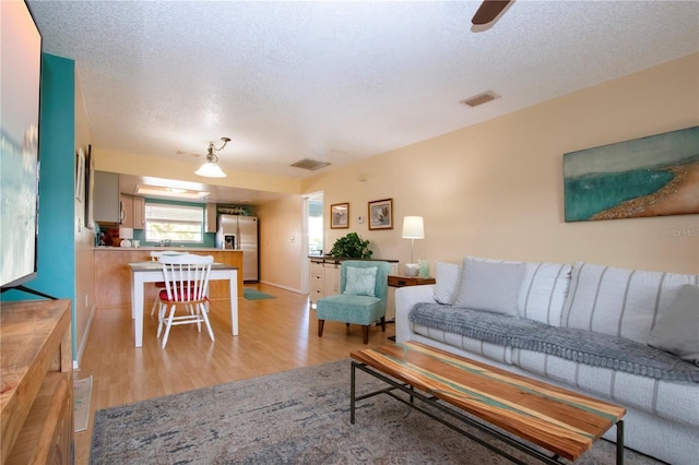 living room with light wood-style floors, visible vents, a textured ceiling, and baseboards