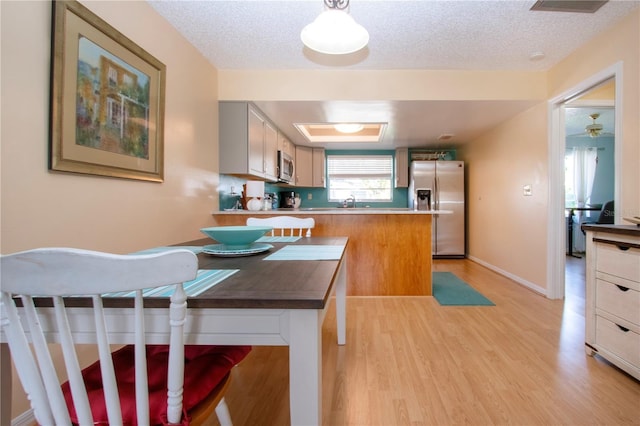 kitchen with stainless steel appliances, light wood-style floors, a textured ceiling, a peninsula, and baseboards