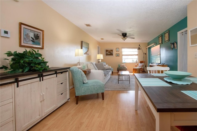 living area with a textured ceiling, visible vents, light wood-type flooring, and a ceiling fan