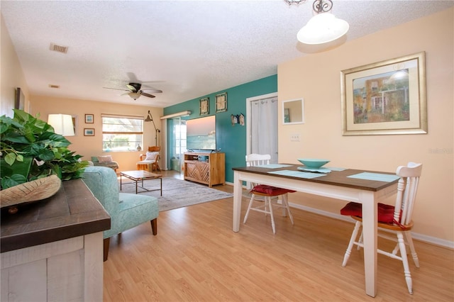 dining room featuring a ceiling fan, baseboards, light wood-style flooring, and a textured ceiling