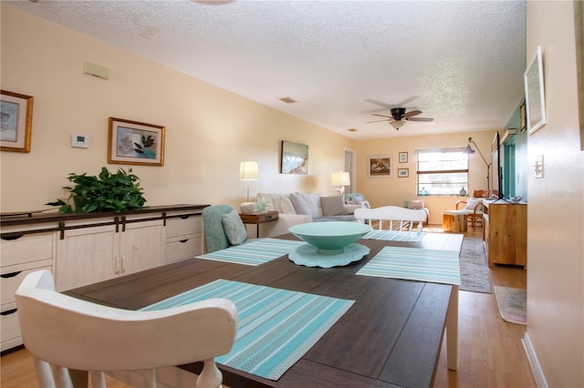 dining space featuring light wood-style floors, visible vents, ceiling fan, and a textured ceiling