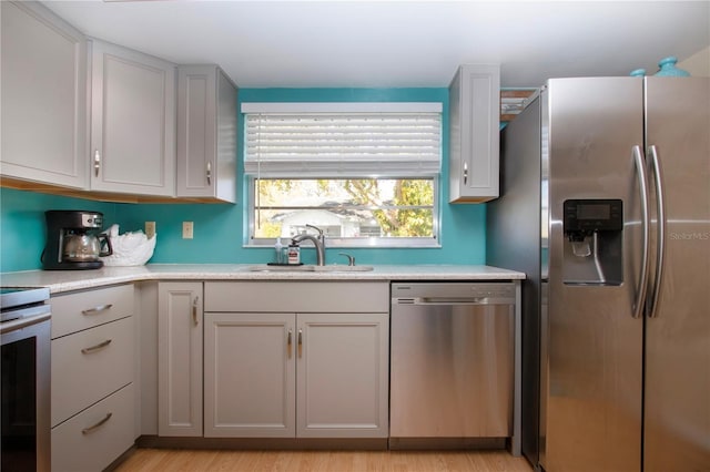 kitchen with gray cabinets, light countertops, appliances with stainless steel finishes, light wood-style floors, and a sink