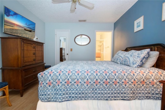 bedroom featuring light wood finished floors, visible vents, a ceiling fan, ensuite bath, and a textured ceiling