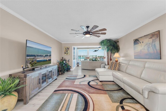 living room featuring a textured ceiling, light wood-style floors, a ceiling fan, and crown molding