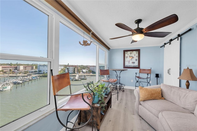 living area with a textured ceiling, a barn door, wood finished floors, a ceiling fan, and crown molding