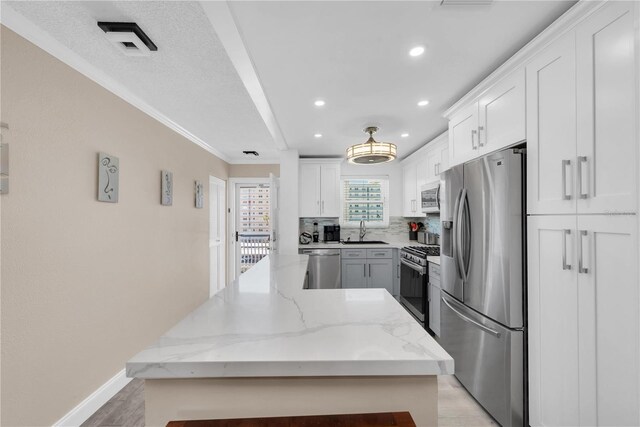 kitchen with stainless steel appliances, decorative backsplash, white cabinetry, a sink, and a kitchen island