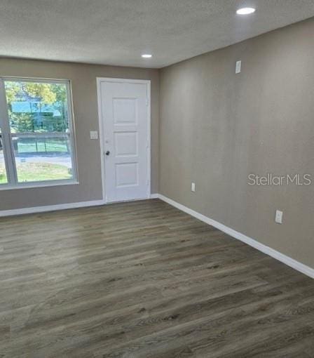 spare room featuring dark wood-style flooring, a textured ceiling, and baseboards