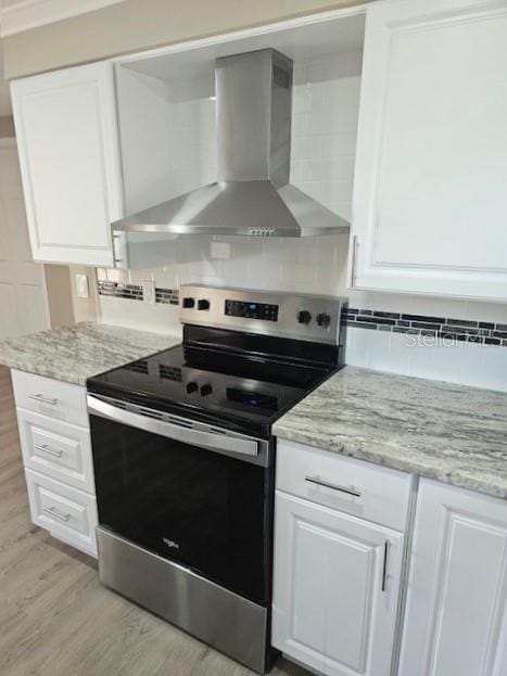 kitchen with white cabinets, electric stove, wall chimney range hood, light wood-type flooring, and tasteful backsplash