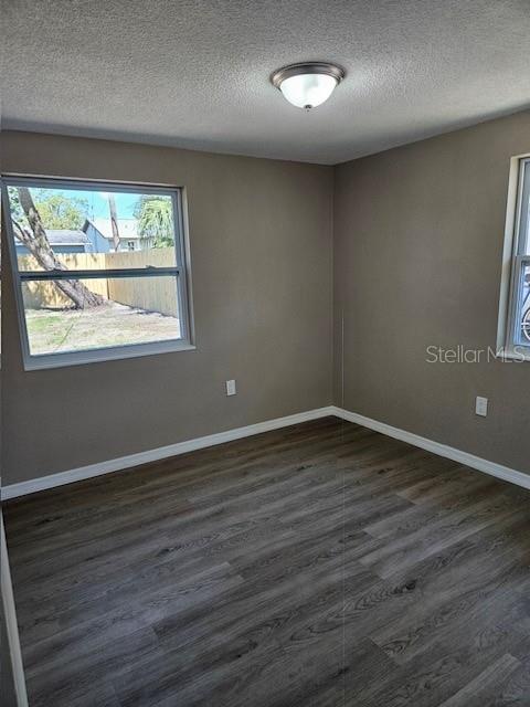 empty room with dark wood-type flooring, a textured ceiling, and baseboards