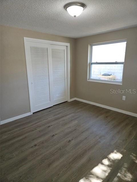 unfurnished bedroom featuring a closet, baseboards, a textured ceiling, and dark wood-style flooring