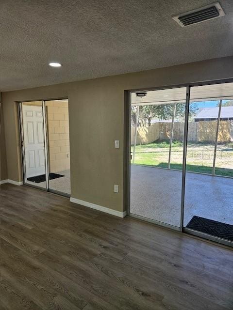 interior space with baseboards, a textured ceiling, visible vents, and dark wood-type flooring