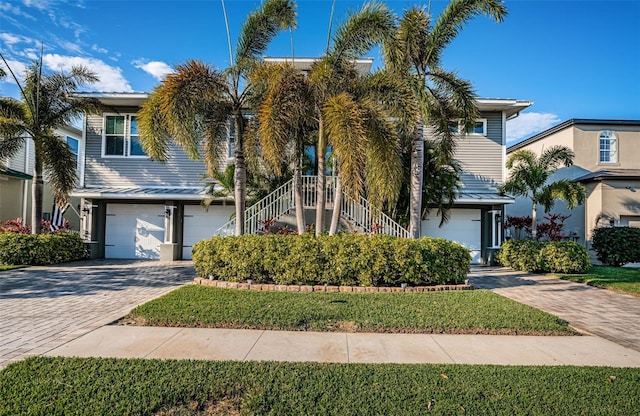 view of front of home with a front lawn, decorative driveway, stairway, and an attached garage