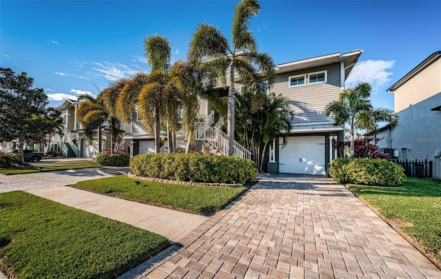 view of front of home featuring stairs, a front lawn, decorative driveway, and an attached garage