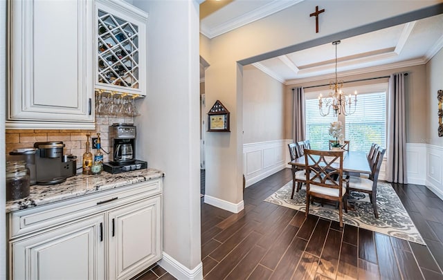 dining room featuring crown molding, a raised ceiling, dark wood finished floors, and wainscoting