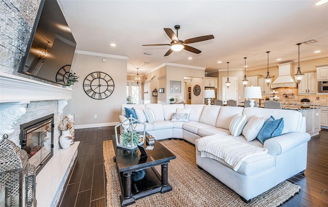 living room featuring ceiling fan with notable chandelier, a fireplace, baseboards, dark wood-style floors, and crown molding