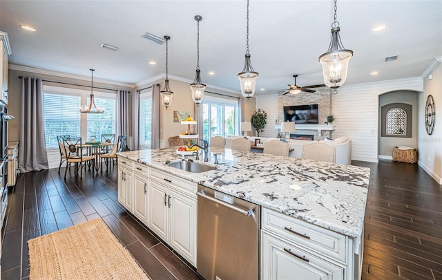 kitchen with appliances with stainless steel finishes, wood tiled floor, ornamental molding, a sink, and a stone fireplace