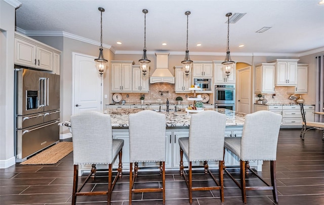 kitchen featuring visible vents, custom range hood, light stone counters, stainless steel appliances, and a sink