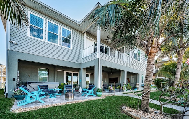 rear view of house with a balcony, a ceiling fan, a yard, stucco siding, and a patio area