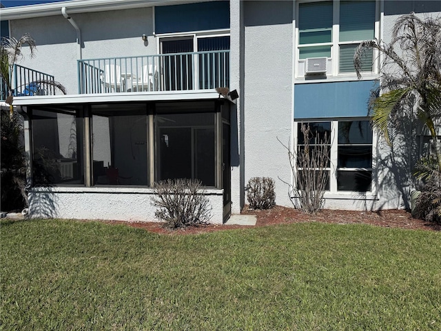 rear view of property featuring a yard, a balcony, and stucco siding