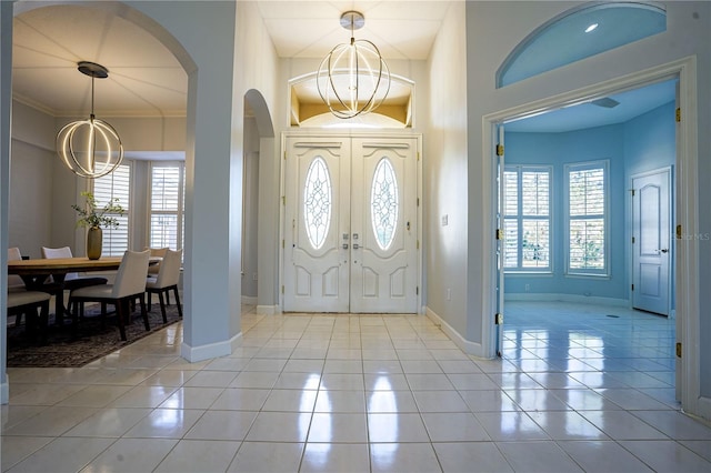 entryway featuring arched walkways, an inviting chandelier, light tile patterned flooring, crown molding, and baseboards