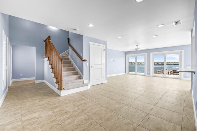 unfurnished living room with visible vents, baseboards, ceiling fan, a water view, and stairs