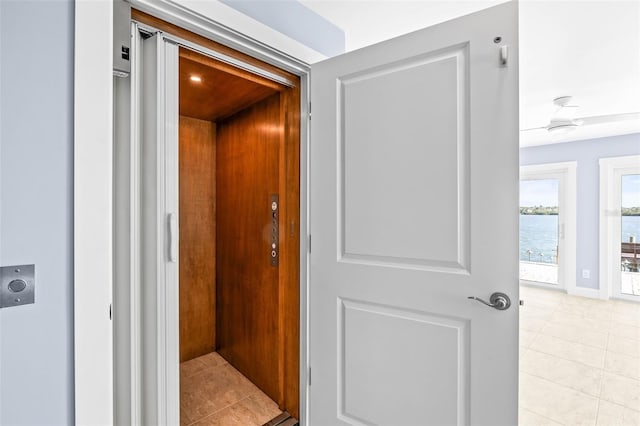 corridor featuring elevator, a water view, and light tile patterned floors