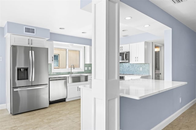 kitchen featuring visible vents, a sink, decorative backsplash, stainless steel appliances, and white cabinets