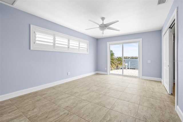 unfurnished room with visible vents, baseboards, ceiling fan, a water view, and tile patterned floors