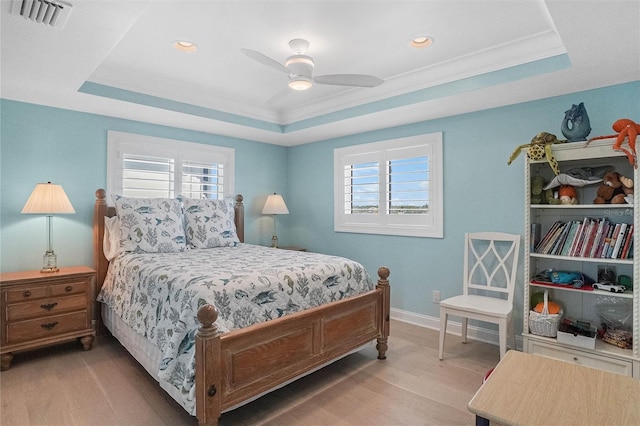 bedroom with light wood-type flooring, visible vents, baseboards, a raised ceiling, and ceiling fan