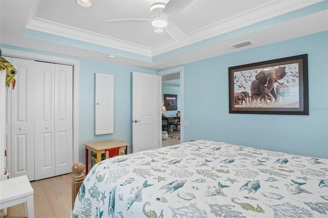 bedroom featuring light wood-type flooring, visible vents, ornamental molding, a tray ceiling, and a closet