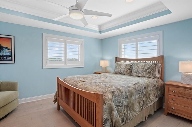 bedroom with a ceiling fan, wood finished floors, baseboards, a tray ceiling, and ornamental molding