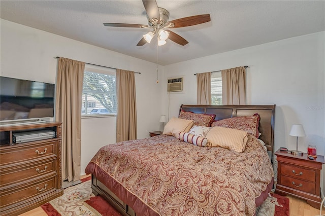 bedroom featuring light wood-style flooring, a ceiling fan, and a wall unit AC