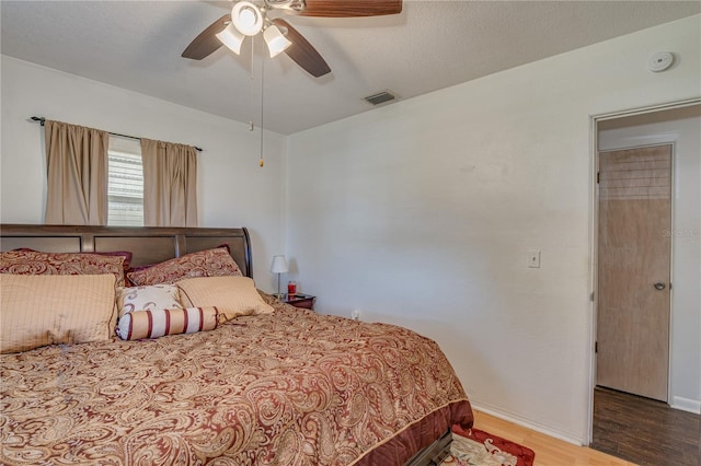 bedroom with ceiling fan, visible vents, baseboards, and wood finished floors