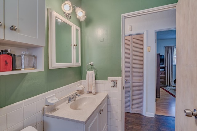 bathroom with vanity, wood finished floors, a wainscoted wall, a closet, and tile walls