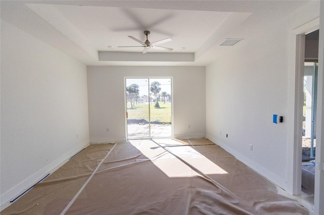 empty room featuring visible vents, a raised ceiling, a ceiling fan, and baseboards