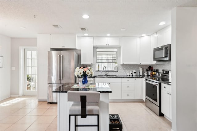 kitchen featuring dark countertops, visible vents, tasteful backsplash, appliances with stainless steel finishes, and a sink