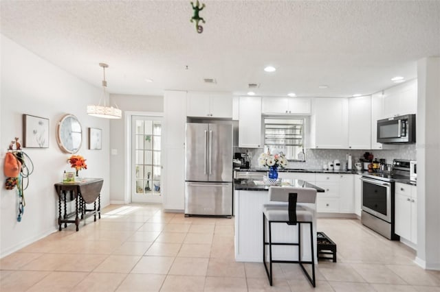 kitchen featuring dark countertops, tasteful backsplash, a kitchen island, appliances with stainless steel finishes, and white cabinetry