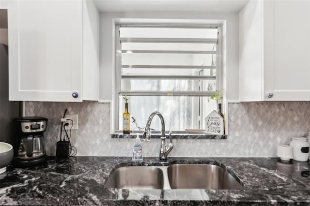 kitchen with dark stone countertops, white cabinetry, and a sink