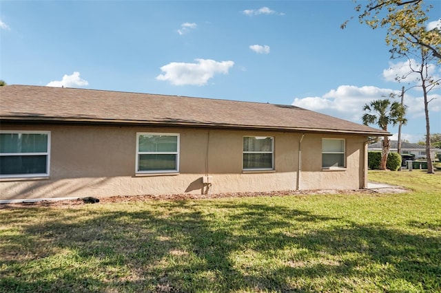 view of side of home with stucco siding, a lawn, and roof with shingles