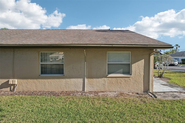 view of side of home with stucco siding, a yard, and a shingled roof