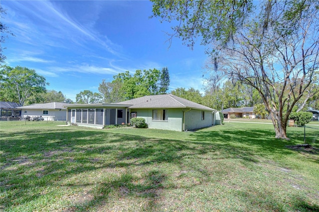 rear view of property featuring a lawn, a sunroom, and stucco siding